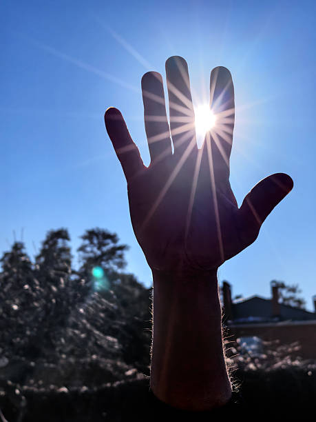 istock Hand reaching towards the sun with bright flare against blue sky 2209418747