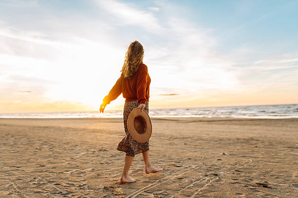istock A beautiful woman with a hat walks on the beach at sunset. 2209422565