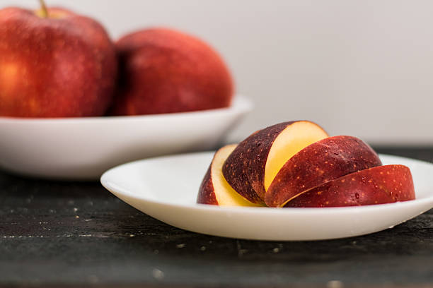 close up of four red fresh apples on a green plate on a colourful table cloth
