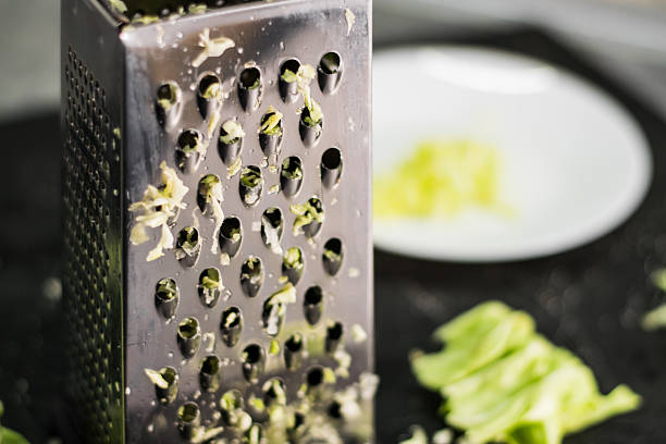 Cabbage after grating lies on the kitchen countertop alongside the grater. The shredded green of the cabbage looks delicate and natural. The kitchen scene with cabbage and grater conveys a sense of freshness and homely comfort.
