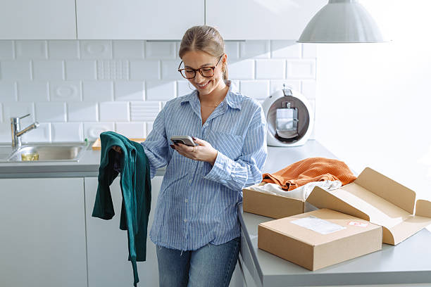 istock Woman inspecting delivered clothing in kitchen while using a smartphone 2209434005