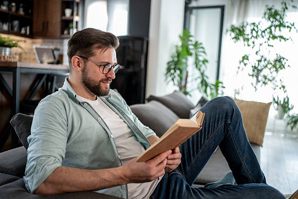 istock Young man relaxing on sofa reading a book at home 2209434902