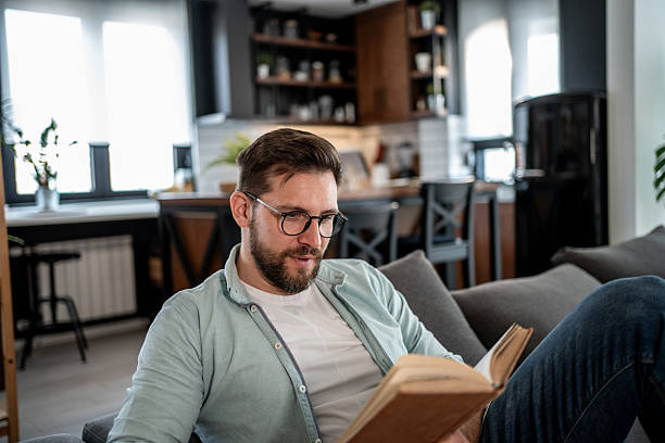 istock Young man relaxing on sofa reading a book at home 2209434905