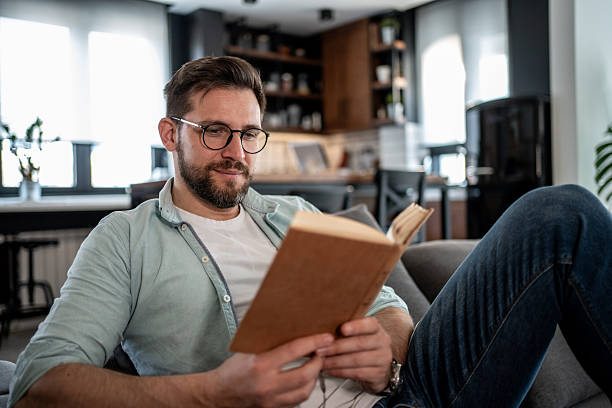 istock Man reading a book at home on the sofa 2209434918