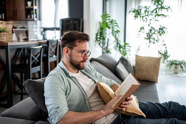 istock Man reading a book on the sofa at home 2209434920