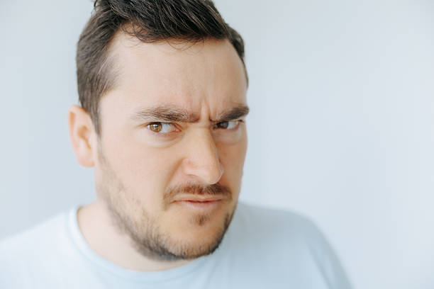 A man displays a confused expression, furrowing his brow in response to something off-screen. The background is plain and bright, highlighting his facial expression.