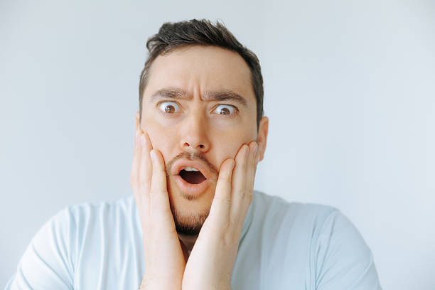 istock Man expressing surprise with hands on face in well-lit indoor setting 2209457310