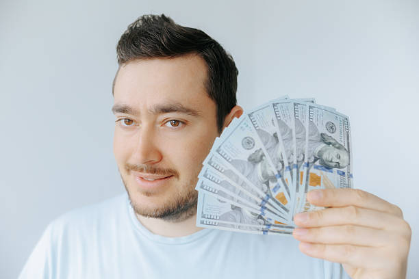 istock Man holding fan of cash with clear expression in bright indoor setting 2209457335