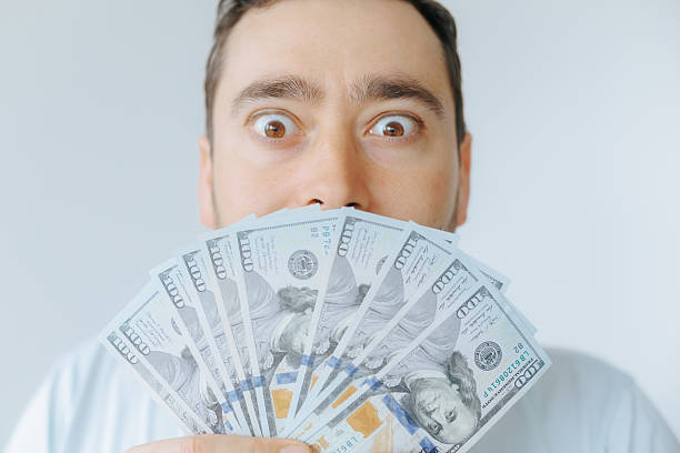 istock Man holding cash with an excited expression in a light-colored setting 2209457372