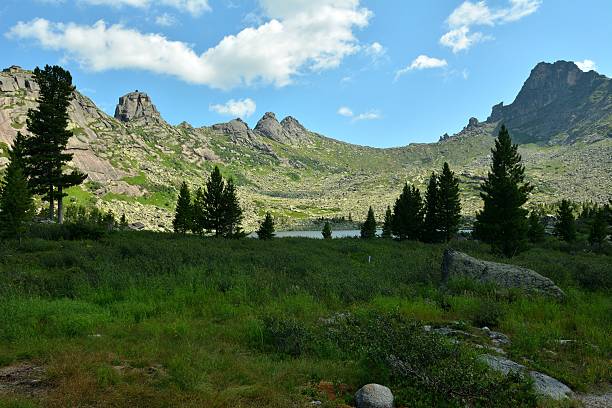 istock A small rocky meadow with several cedars behind which is a lake surrounded by a mountain range on a sunny summer day. 2209459848