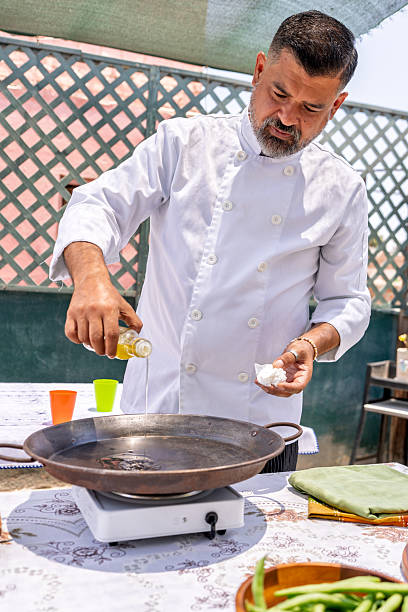 istock Chef pouring olive oil into paella pan on rooftop 2209462323