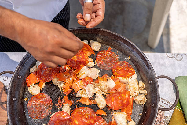Chef adding chorizo to chicken and tomato in paella pan