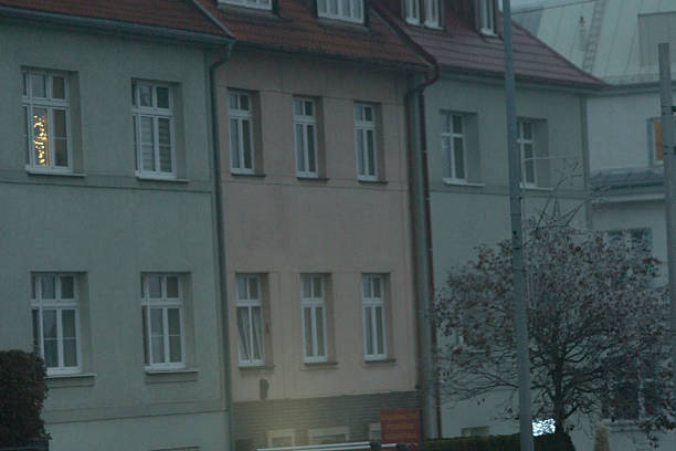 The exterior of a building displays a series of windows within a bustling urban environment, showcasing city life in foggy dusk evening. European city buildings background.