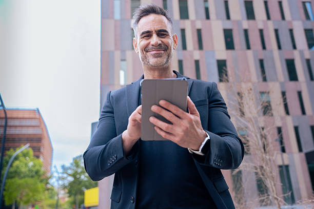 istock Smiling businessman using tablet outdoors in city, confident and modern look 2209472501