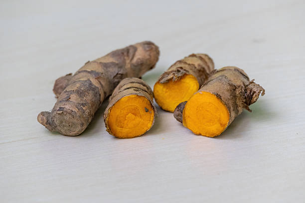 istock Raw turmeric roots, whole and cut in half, on a light wooden surface. 2209474860