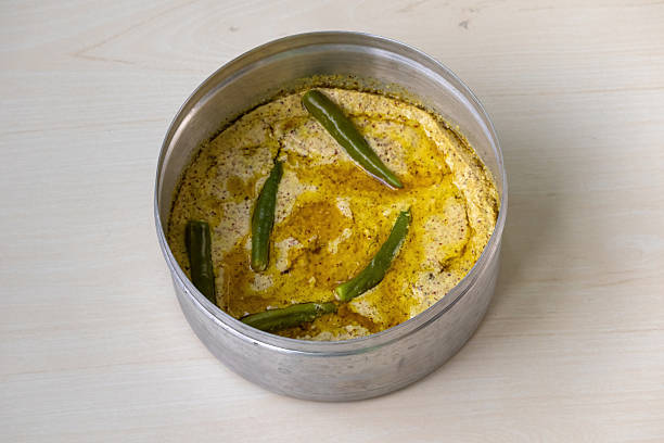 istock Delicious shorshe ilish served on silverware atop a light wooden surface. This popular Bengali dish, made with Hilsa fish, is cooked with mustard seeds. 2209475275