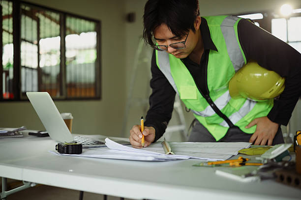 istock Focused engineer in a safety vest working on construction plans at a table 2209476508