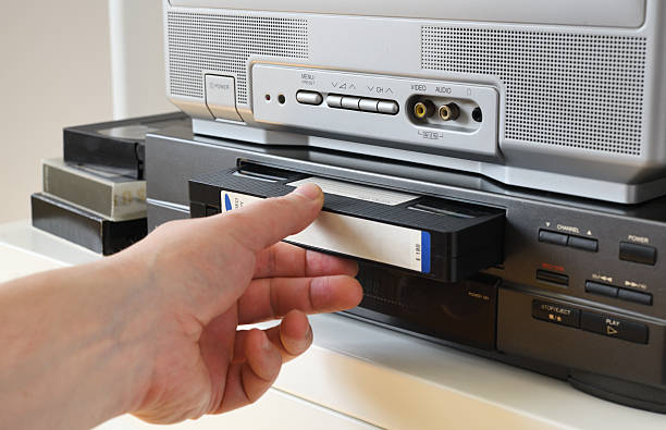 istock Hand inserting a VHS tape into a video cassette player at home 2209486192