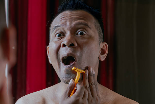 Asian man shaving in bathroom hurting himself. Daily morning routine.