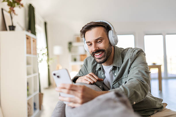 istock Man Lounges on Sofa, Laughing During Headphone Video Chat 2209494584