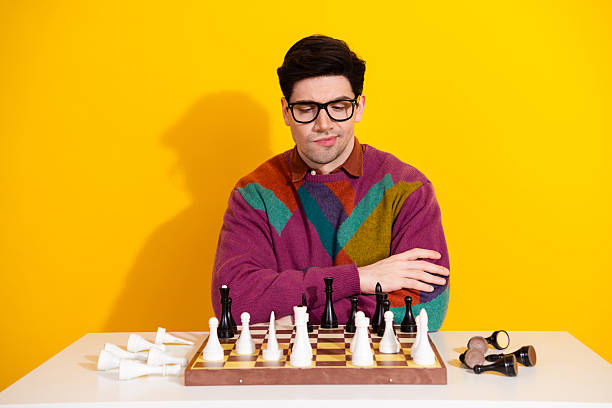 istock Young man contemplating a chess move while seated against a vivid yellow background, exuding a casual and stylish demeanor 2209499054