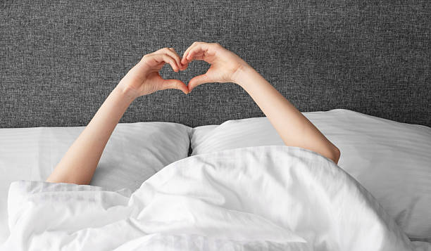 istock Hands forming heart shape above blanket in cozy bed setting with gray headboard. 2209501729