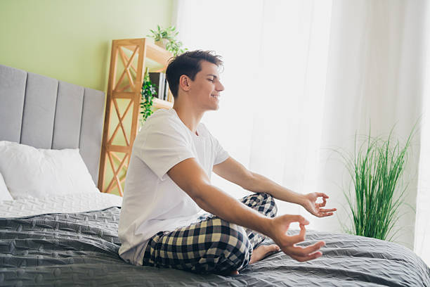 istock Young man practicing meditation on his bed in a bright and comfortable bedroom for relaxation and mindfulness during the day 2209504494