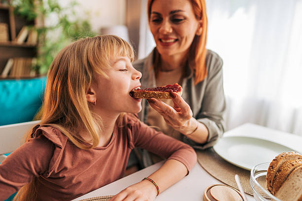 istock Mother feeding her daughter with toast and jam at breakfast time 2209504967