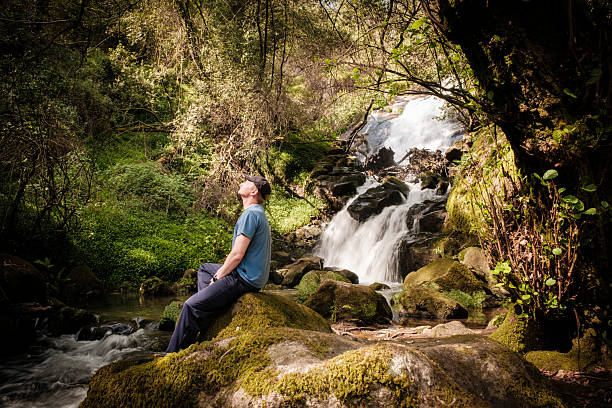 Carefree woman standing by the waterfall with her arms raised during springtime in forest. Photographed in medium format.