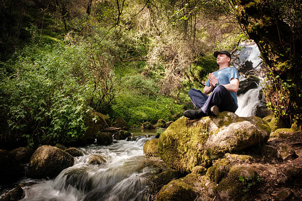 Man enjoying the peace of nature while meditating near a waterfall