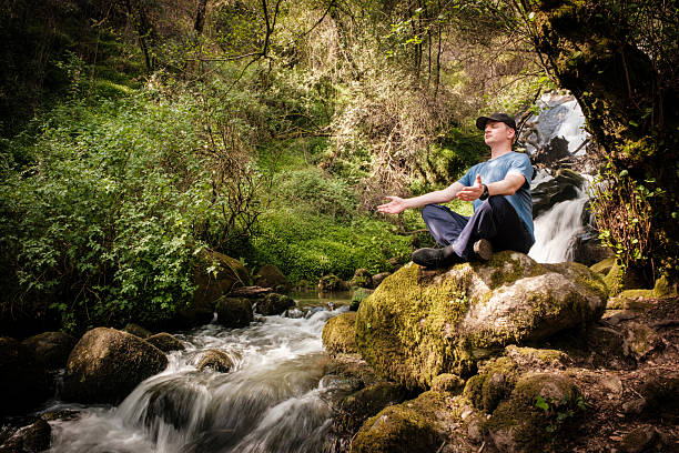 man meditating near a waterfall in a lush green forest, enjoying the peace and tranquility of nature