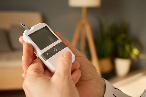 istock A person is holding a glucometer in a comfortable room, preparing to check their blood sugar levels. The background features soft lighting and indoor plants, creating a relaxing atmosphere 2209510526