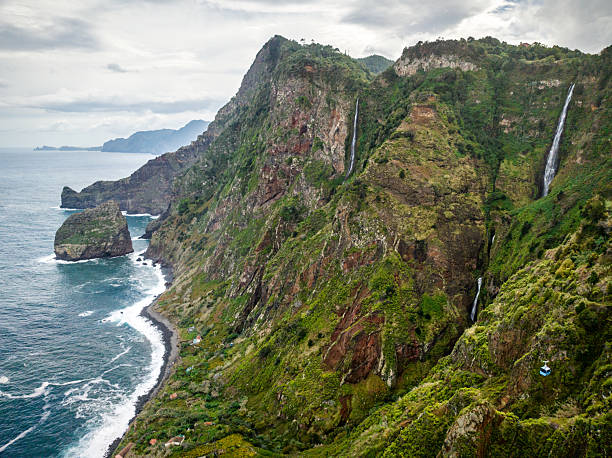 Breathtaking aerial view of Rocha do Navio waterfalls cascading down lush green cliffs on Santana, Madeira Island, Portugal, creating a dramatic and scenic landscape