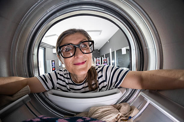 Mature woman taking dry clothes out of machine in  self-service public laundry, photo taken from inside of a machine