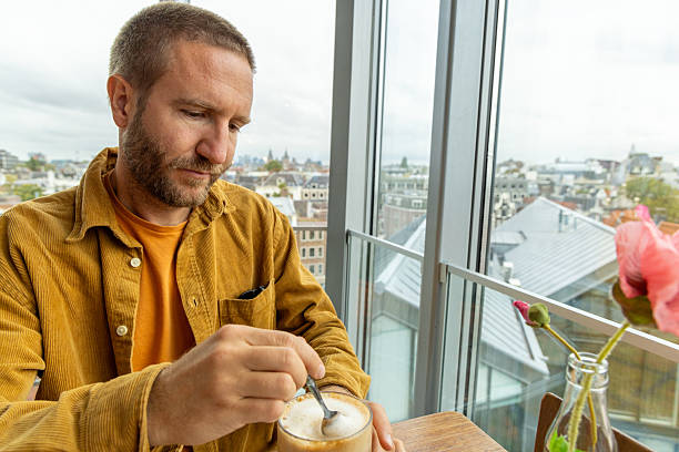 A man enjoys a chai latte in a cafe with Amsterdam city view