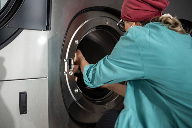 Mature woman putting clothes in washing machine in self-service public laundry