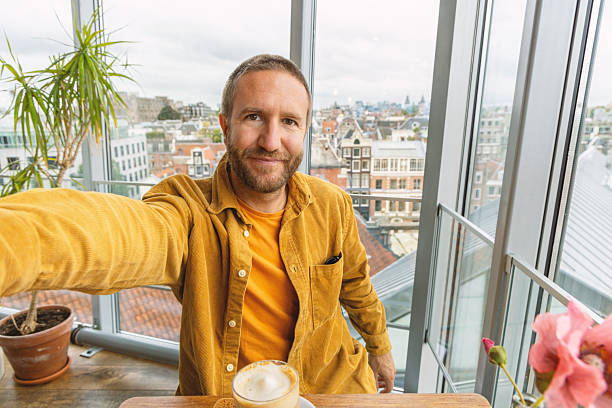 Man Taking Selfie While Enjoying Coffee in Modern Urban Apartment Near Large Window
