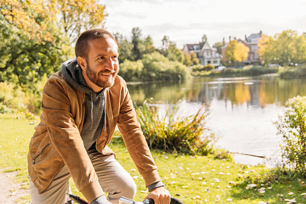 istock Man Cycling Along Leafy Lakeside Park Trail on Sunny Day 2209513633