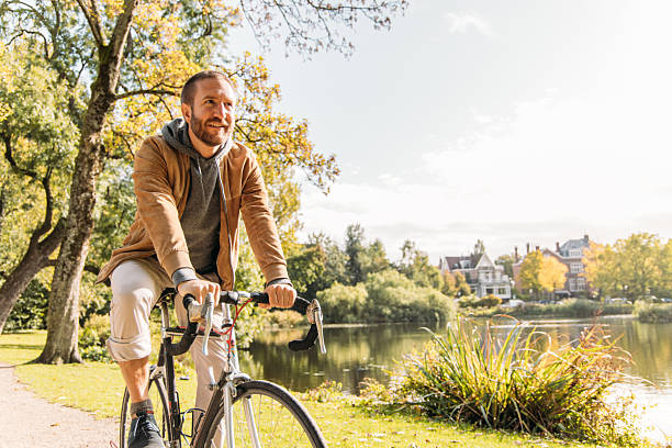 istock Man Cycling Along Leafy Lakeside Park Trail on Sunny Day 2209513640