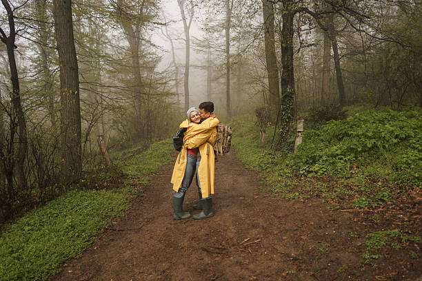 Full length of happy young couple whit backpacks and raincoats kissing in the forest