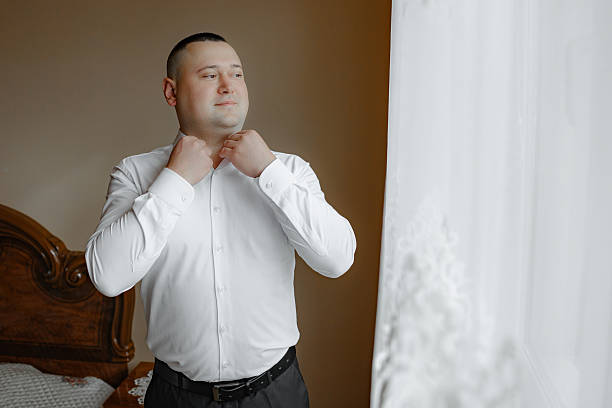 istock A man in a white shirt is getting dressed in front of a window 2209518124