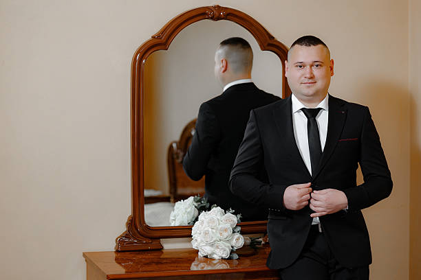 istock A man in a suit stands in front of a mirror, adjusting his tie 2209518253