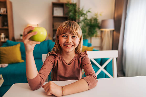 istock Smiling elementary age girl showing green apple at home 2209523007