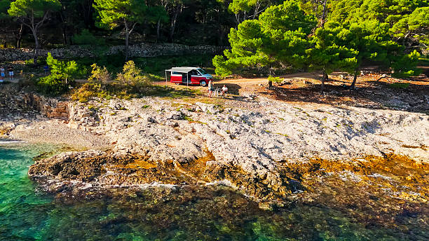 istock Red Camper Van Perched On Rocky Mediterranean Coastline With Crystal Clear Turquoise Waters 2209527003