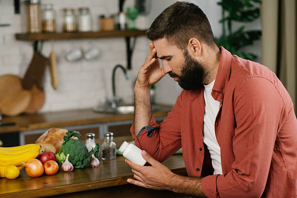 istock Young man sitting at the table and looking at the pill bottle with headache. 2209529139