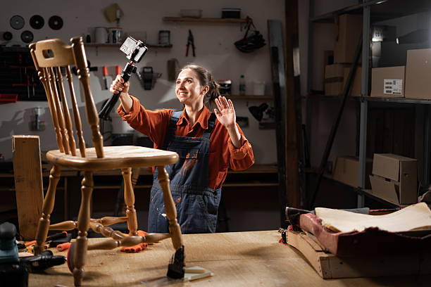 istock Female carpenter holding camera on tripod while recording diy video blog, she restoring old furniture in her workshop. 2209529509