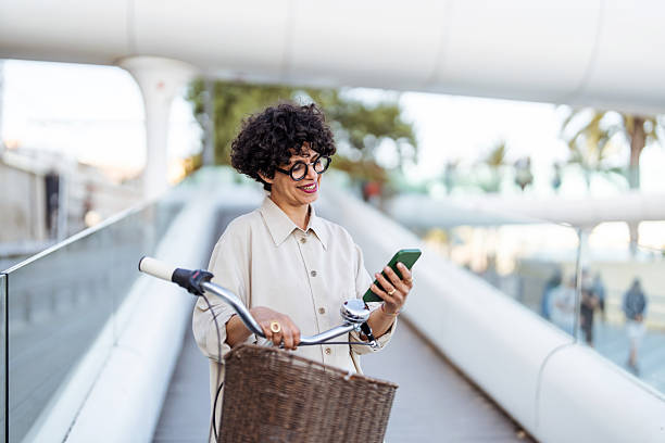 istock Woman Using Smartphone While Pushing Bicycle on Modern Pedestrian Walkway 2209533062