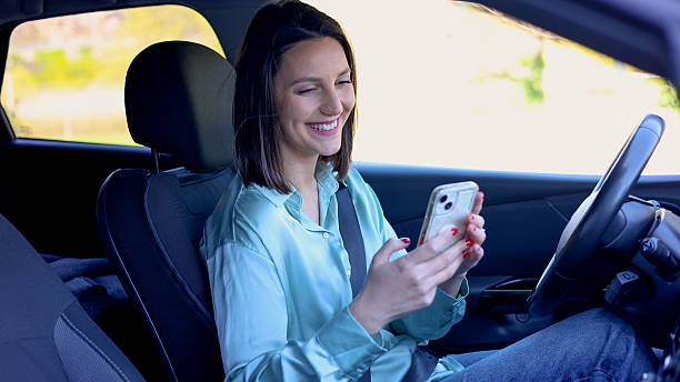 istock Smiling young woman using smartphone while sitting in a car 2209537609