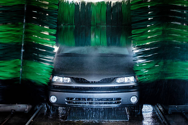 Front view of a grey car being washed in an automatic car wash with green rotating brushes