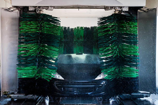 Automated car wash driver's point of view as high pressure sprayed rinsing water rapidly dilutes the car wax solution previously applied and drains in slippery twisting rivulets down the windshield glass.
